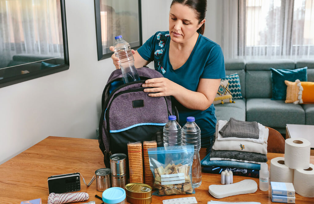 Woman putting emergency supplies from a table into a backpack.