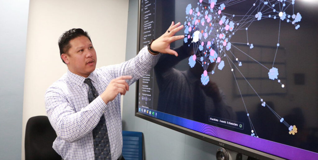 Man standing in front of a monitor displaying a complex relationship diagram.