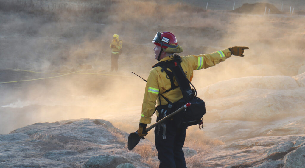 Firefighter standing and pointing in a smoky landscape.