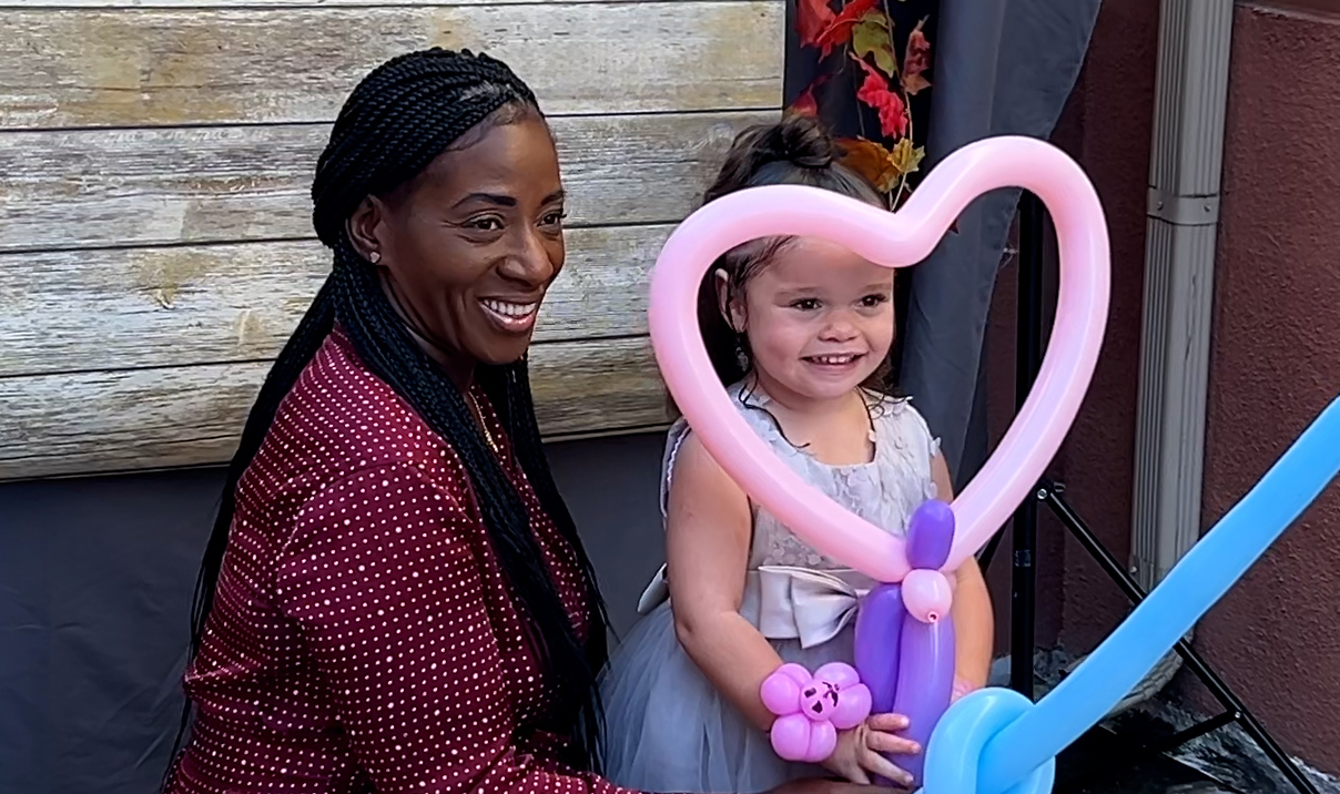 Woman and little girl posing for photo. The girl has a balloon in the shape of a heart framing her face.