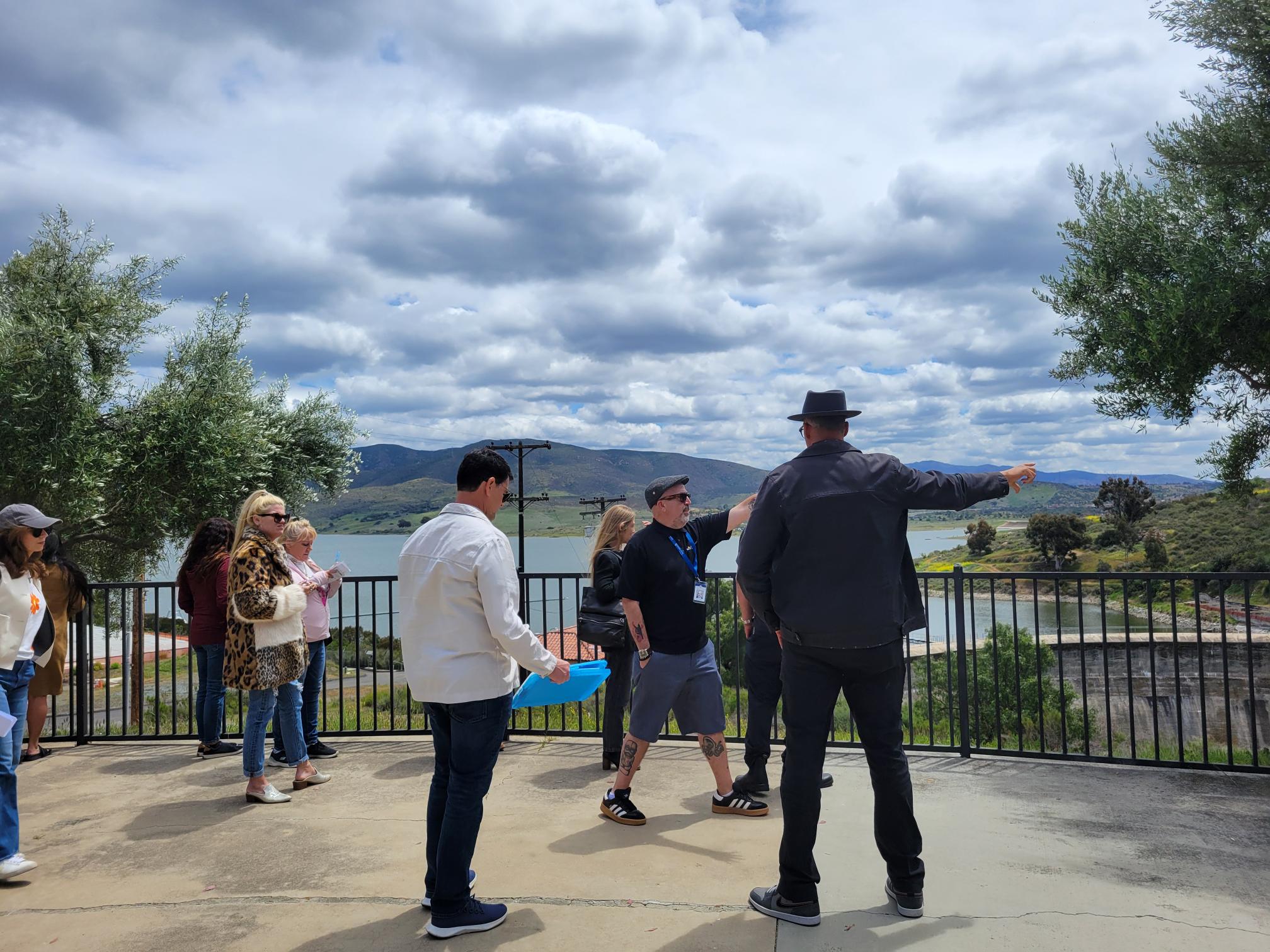 Group of people pointing and looking off to the right. Behind them is a lake.