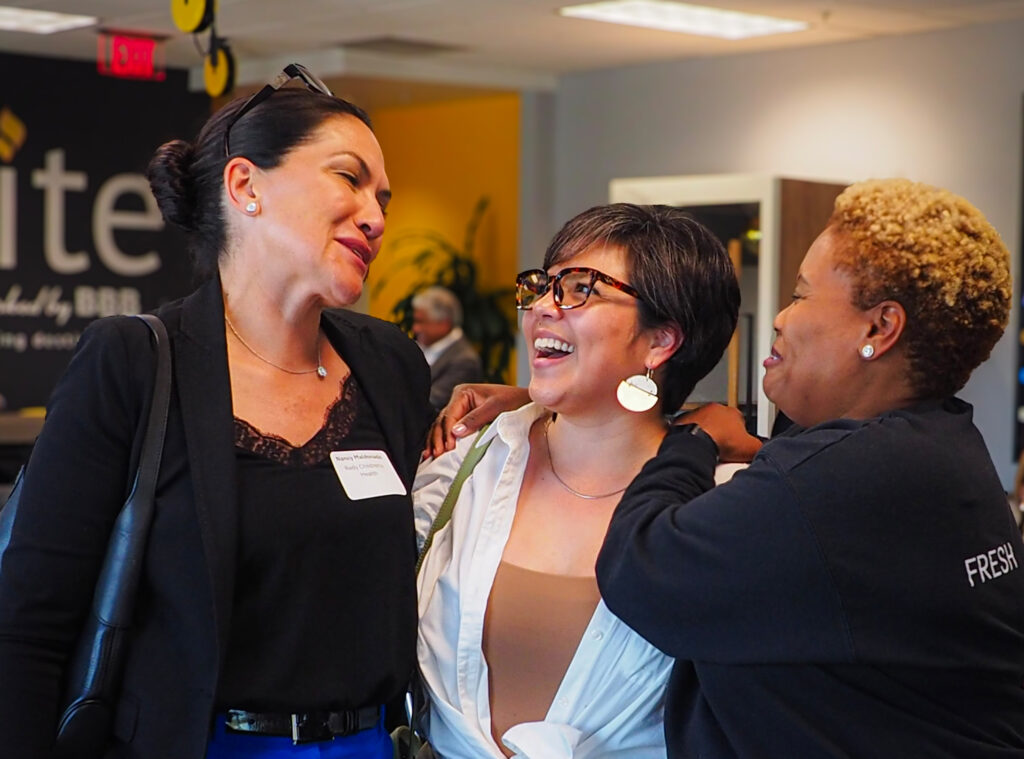 Three women at an indoor event standing close together and laughing.