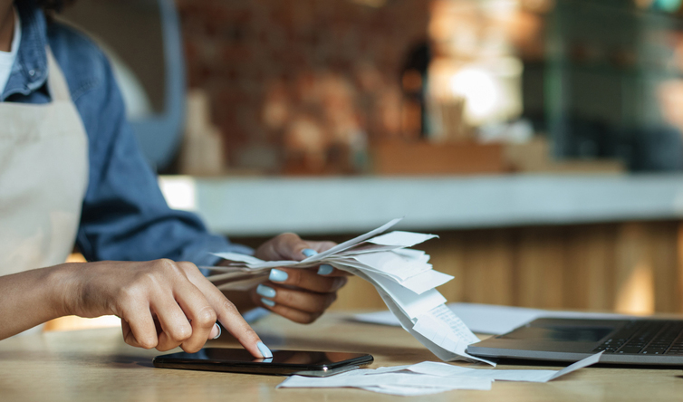 Person holding receipts and using calculator.